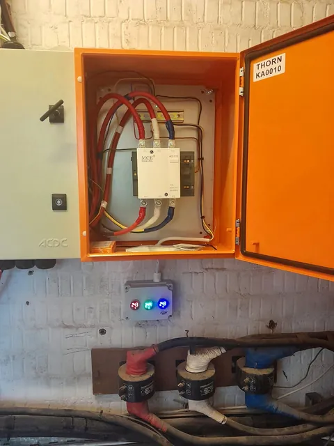 Orange enclosure with a contactor, voltage indicator lights and current transformers on the cables